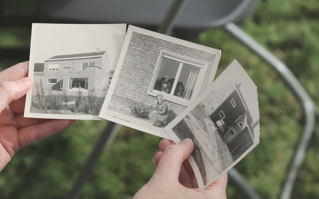 Hände halten alte Fotos eines Hauses.